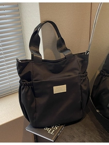Waterproof nylon shoulder bag in black featuring side pockets and webbed handles