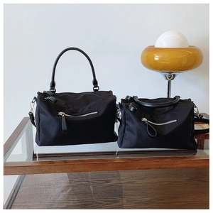 Detail of two black nylon messenger bags with silver zippers on a glass display
