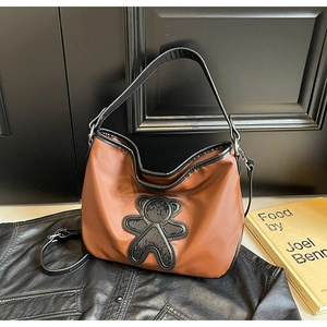 Détail d'un sac à bandoulière marron avec écusson d'ours noir et double sangle de transport