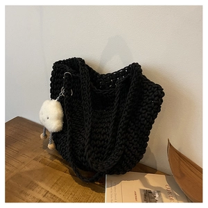 Detail of black hand-woven tote bag texture with cute plush cloud charm on a wooden table