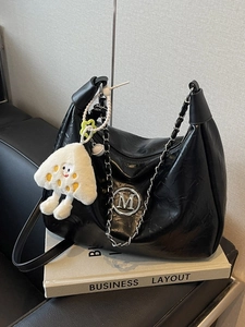 Elegant black wrinkled leather tote with silver M logo and plush charm on white books