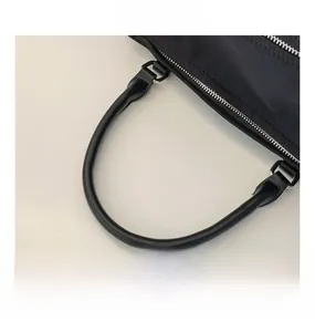 Detail of black nylon bag featuring leather top handles and smooth metal dual zippers
