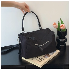 Detail of black nylon crossbody bag with silver zipper and round handle on books