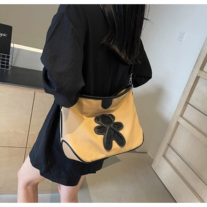 Sac bandoulière jaune moutarde avec écusson ours, porté par un modèle en extérieur