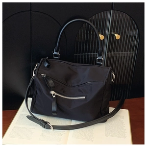 Detailed shot of a black nylon crossbody bag featuring dual silver front zippers and handle