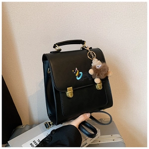 Detail of black PU leather backpack with gold buckles and cute teddy bear charm