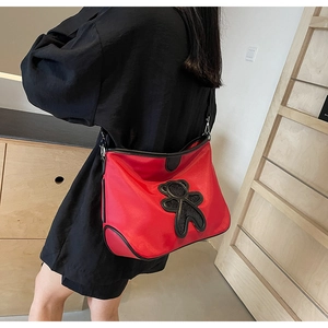 Détail du sac de voyage rouge léger avec écusson ours noir et bandoulière réglable