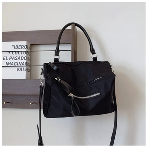Close-up of black nylon crossbody bag with silver zippers and leather handles on a shelf