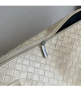 Detail of woven beige leather tote bag featuring a smooth silver metal zipper head