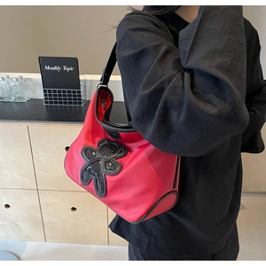Détail d'un sac de voyage léger en nylon rouge avec un patch ours en paillettes noires et sangle