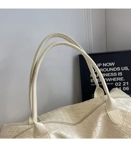 Detail of reinforced handles and woven leather texture on a cream white tote travel bag