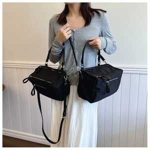 Detail view of black nylon box bags in two sizes with multiple silver zippers and leather handles