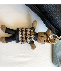 Detail view of a knitted teddy bear charm with houndstooth sweater on a black leather bag