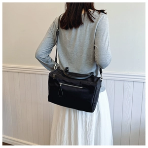 Detail of black nylon messenger bag featuring silver zipper and adjustable shoulder strap