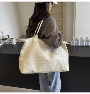 Detailed close-up of a cream woven tote bag with reinforced curved edges and wide grid pattern