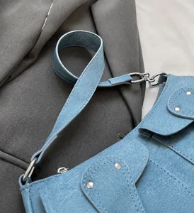 Detail der hellblauen Denim-Schultertasche mit breitem Griff und Metallnieten-Akzenten