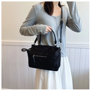 Detailed view of lightweight black nylon crossbody bag with silver zipper and top handles