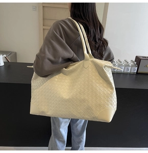 Detail of woven cream tote bag with reinforced corners shown in a lifestyle street setting
