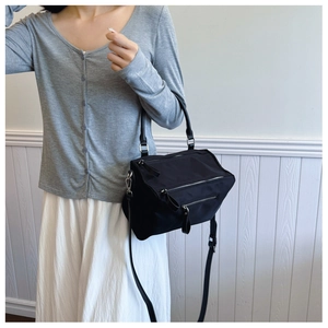 Detail of a black nylon crossbody bag featuring double parallel zippers and a top handle