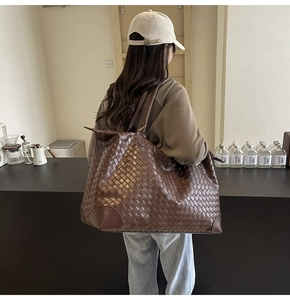 Detail of a dark brown woven tote bag featuring high-quality leather and dual top handles