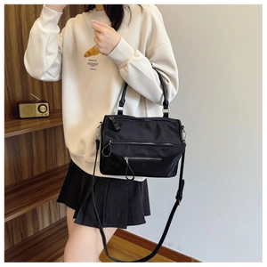 Detail of a black nylon crossbody bag with triple zippers shown in a lifestyle setting