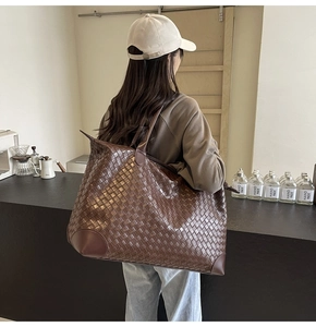 Detail of large woven tote bag in dark brown showing texture and capacity on shoulder