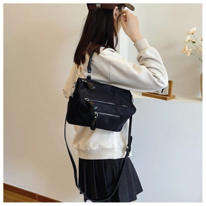 Detail of high-density black nylon crossbody bag with silver zippers and long leather pulls
