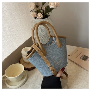 Detail of blue denim bucket bag with brown leather handles and golden logo hardware