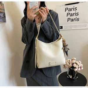 Close-up of white pebble leather bucket bag with cute plush rabbit charm and metal logo