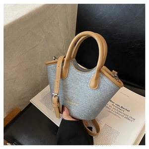 Detailed view of woven fabric bucket bag with brown leather handle and gold lettering