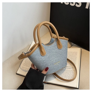 Detail of blue denim bucket bag featuring brown leather handles and gold logo accents