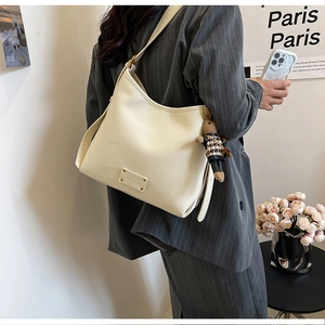 Detail of cream pebbled leather bucket bag with cute bunny charm and wide shoulder strap