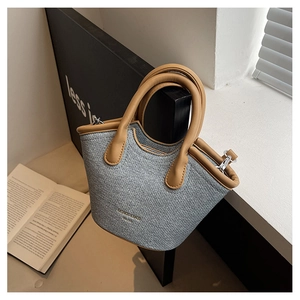 Detail of grey textured bucket bag with brown leather handles and 1985 text