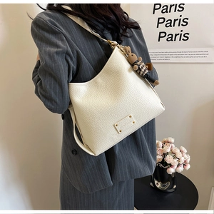 Side view of beige leather bucket bag with plaid rabbit charm on gray striped blazer