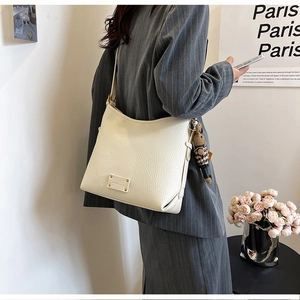 Close-up of beige lychee leather bucket bag with a cute bear charm and rivet detail