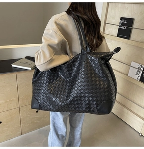 Macro shot of large black woven tote bag showing the detailed intrecciato weave pattern