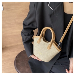 Detailed view of woven straw mini bucket bag with brown leather handles and gold hardware
