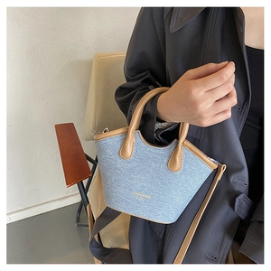 Close-up of light blue denim bucket bag featuring camel leather trim and fashion lettering
