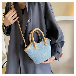 Model wearing a mini light blue denim bucket bag with brown leather trim and shoulder strap