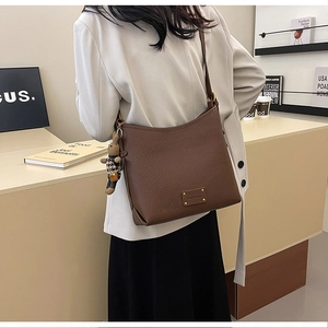 Brown lychee leather bucket bag detail with cute bunny charm on model's shoulder