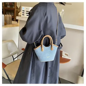 Detail view of denim bucket bag with brown leather handles worn by a model in a cafe