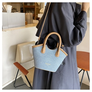Detail of light blue denim tote bag with brown leather handles worn by a model in a cafe