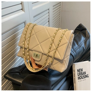 Detail of beige quilted shoulder bag with gold chain strap held by a model