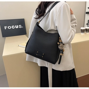 Detail of black lychee grain leather bucket bag with gold clasp and bear charm on model