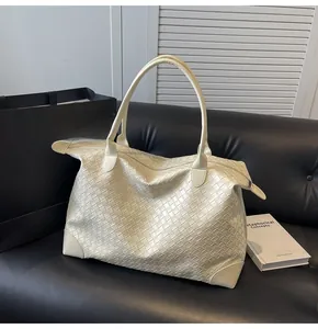 Close-up of woven cream tote bag detailing Intrecciato texture on a black sofa