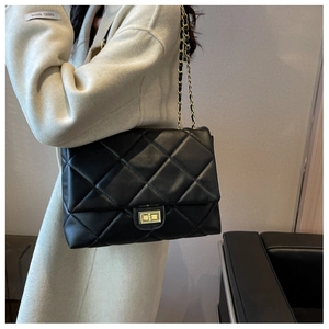 Side view of black quilted shoulder bag with gold chain strap worn by a model