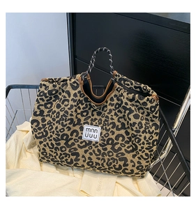 Detail of leopard print tote bag with woven handles and brand label on fabric texture