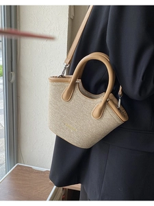 Champagne woven bucket bag with leather handles shown from a stylish side view angle