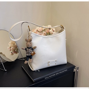 Detail of white lychee leather bucket bag with cute rabbit charm and metal logo plate