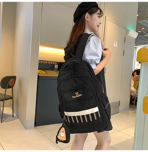 Détail d'un grand sac à dos noir pour étudiant avec slogan jaune et breloque pizza mignonne